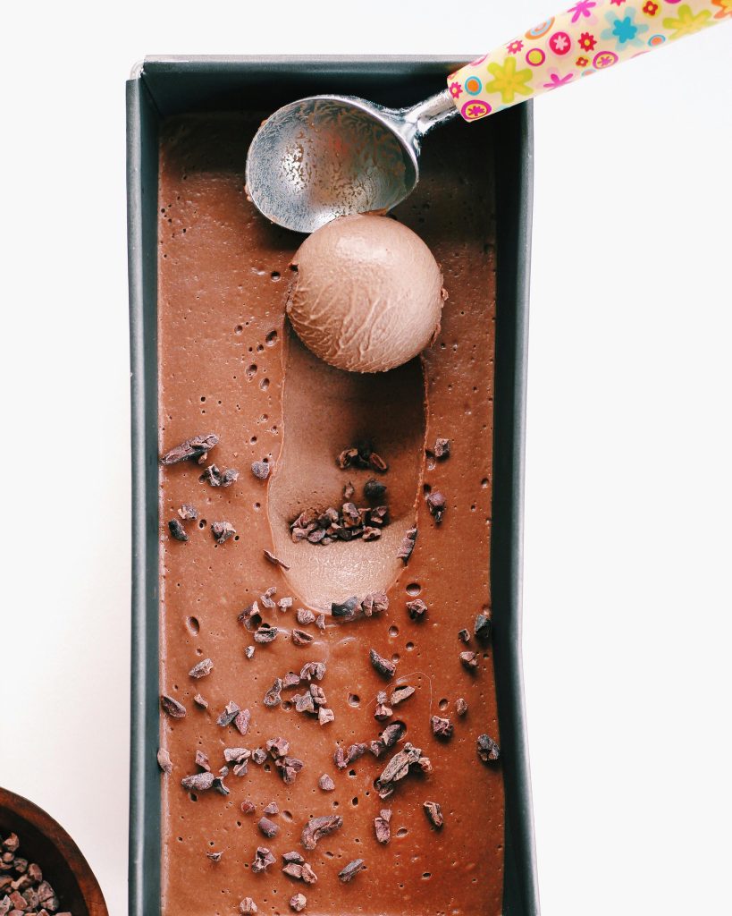 pexels-photo-1346341-1346341 Delicious homemade chocolate ice cream in a tray with a colorful scoop, garnished with cacao nibs.